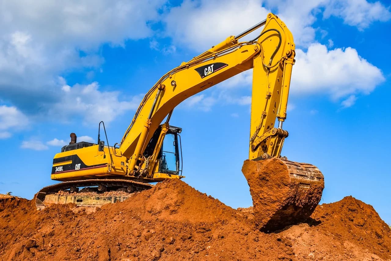 An excavator digging into a pile of red dirt