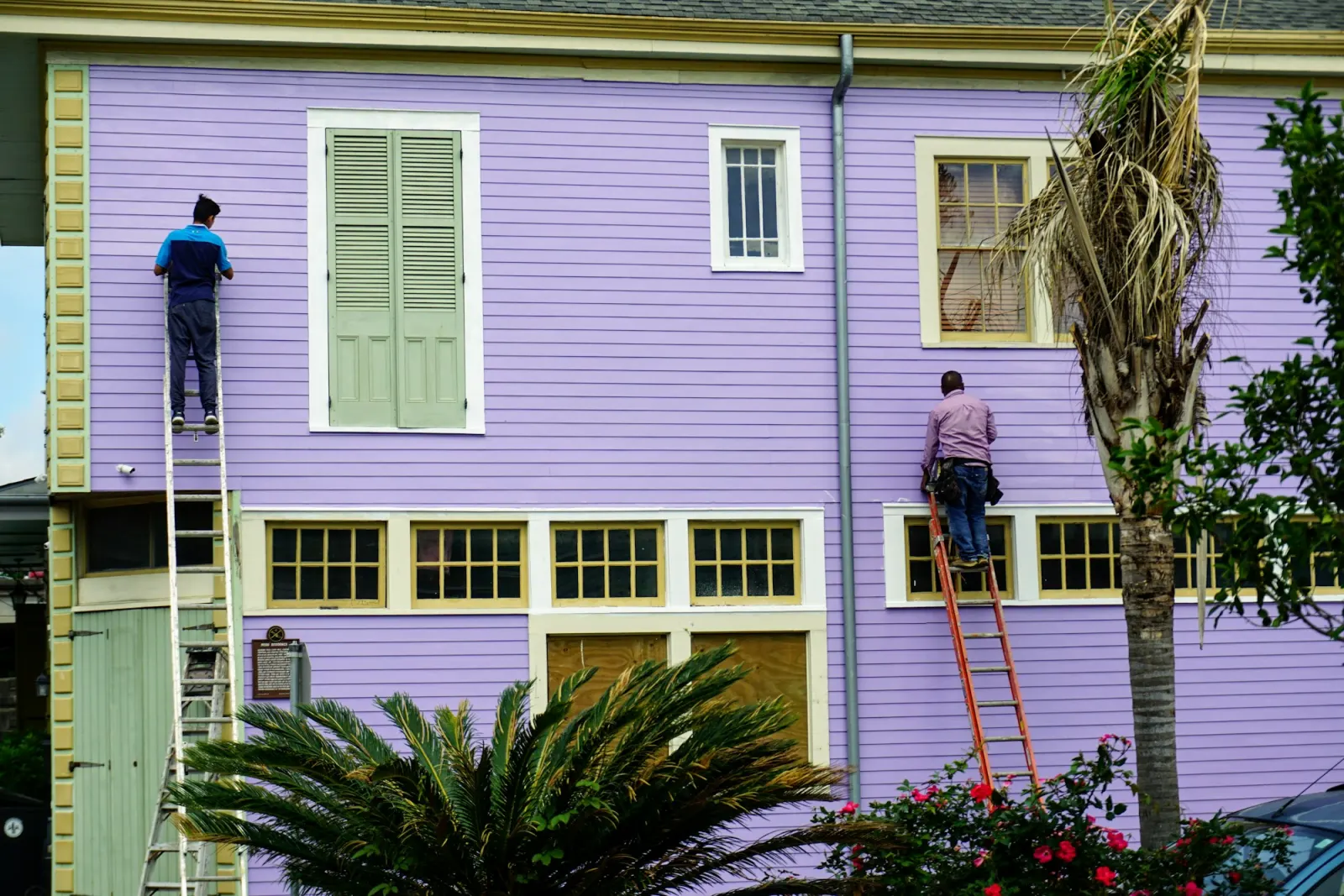 Two painters on ladders painting a house exterior